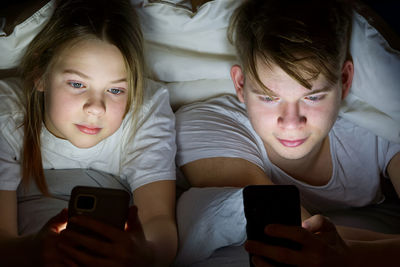 Portrait of siblings using mobile phone under blanket