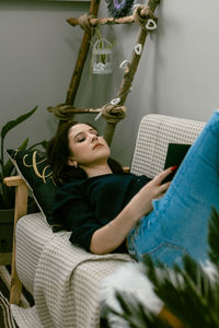 Portrait of young woman using mobile phone while sitting on sofa at home