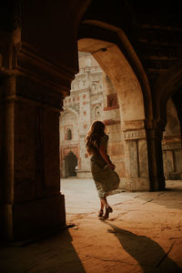 Full body back view of anonymous female tourist running under arched passage of muhammad shah sayyid tomb at lodhi garden in new delhi