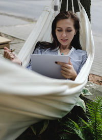 Young woman drawing on sketch pad while lying in hammock