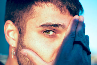 Close-up portrait of man covering face with hand standing outdoors