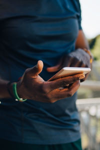 Midsection of sportsman using mobile phone while standing on bridge