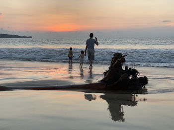 Men on beach against sky during sunset