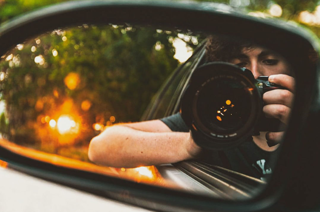 reflection, one person, camera - photographic equipment, photography themes, photographing, photographic equipment, camera, mode of transportation, holding, technology, mirror, portrait, motor vehicle, close-up, car, leisure activity, headshot, selective focus, side-view mirror, real people, outdoors, digital camera, teenager