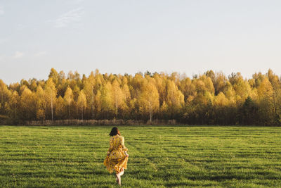 Mid adult woman walking on grass in autumn field on sunny day