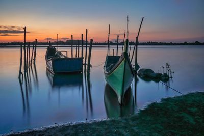 Sailboats moored in lake against sky during sunset