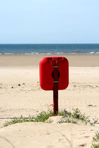 Red wooden post on beach against sky