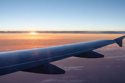 Airplane wing against sky during sunset