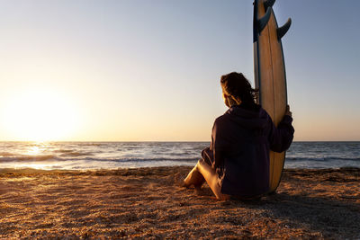 Rear view of man looking at sea against sky during sunset