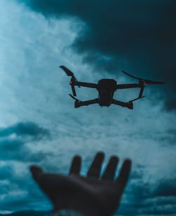 Close-up of person with drone flying against sky at dusk