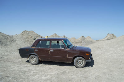 Vintage car on desert land against clear blue sky