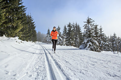 Woman running on snow covered field against sky