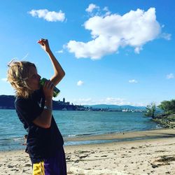Rear view of girl standing on beach against sky