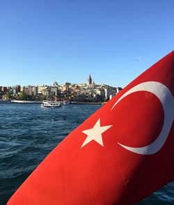 Red flag against buildings in city against clear blue sky