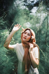 Young woman looking away while gesturing against trees