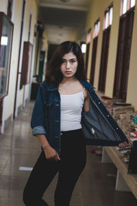Portrait of confident young woman wearing denim jacket standing in corridor
