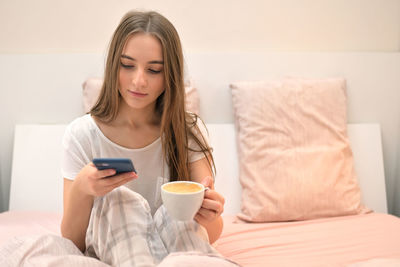 Young woman holding coffee cup on bed at home