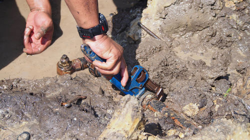 Cropped hands of man repairing pipe in mud