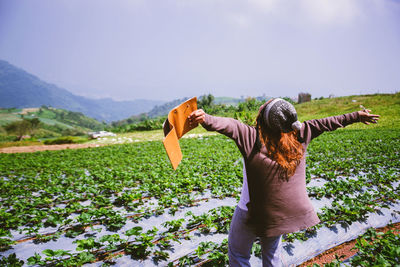 Rear view of woman with arms outstretched standing on field against sky