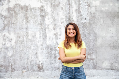 Portrait of a smiling young woman standing against wall