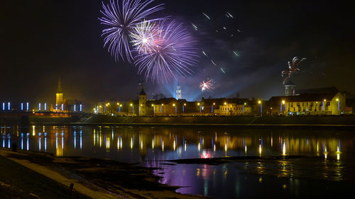 Firework display over river by buildings against sky at night