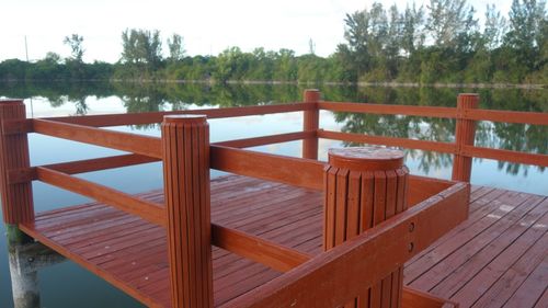 Wooden railing by lake against sky