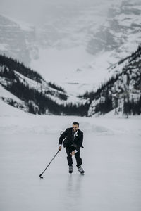 Man in suit plays hockey on frozen lake louise, alberta, canada