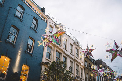 Low angle view of star shape decorations hanging by buildings against sky