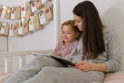 Mather with toddler child reading book or photo album on christmas eve near eco advent calendar in