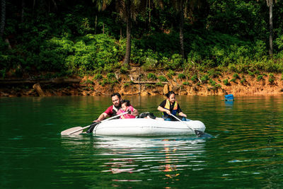 Family wearing life jackets paddling on an inflatable boat in kenyir lake, malaysia.