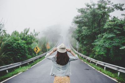 Rear view of woman standing on road amidst trees