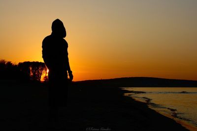 Silhouette man standing on beach against sky during sunset