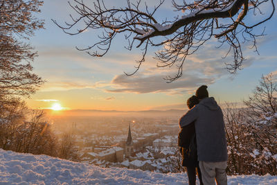 Rear view of man standing on snow field against sky during sunset