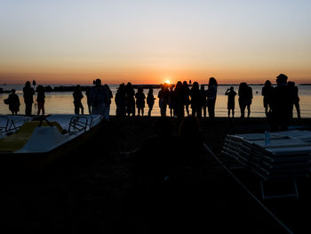 Silhouette people standing on beach against sky during sunset