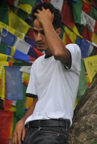 A good looking indian young guy poses outside with buddhist prayer flags in the background
