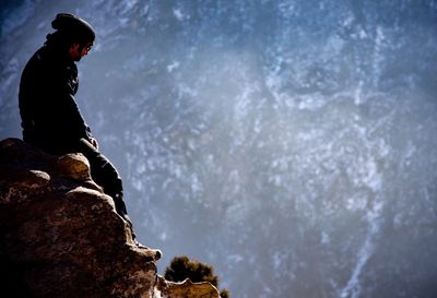 Low angle view of person standing on rock against sky