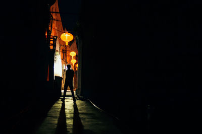 Rear view of a boy silhouette walking on illuminated street at night