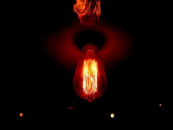 Low angle view of illuminated lighting equipment against black background