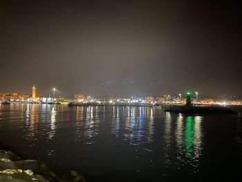 Illuminated buildings by river against sky at night