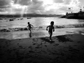 Silhouette people playing soccer on beach against sky