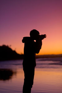 Silhouette man standing at beach against sky during sunset