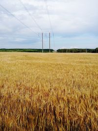 Low angle view of electricity pylon in field against cloudy sky