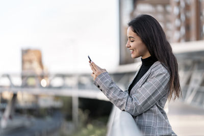 Side view of young smiling woman using mobile phone