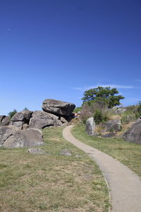 Road by rocks against clear blue sky
