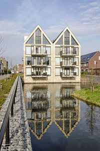 House-shaped apartment building with brick and glass facade, reflecting in a pond