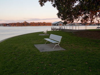 Empty chair on field by sea against sky