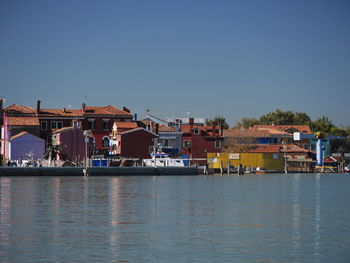 Houses by river against buildings against clear sky