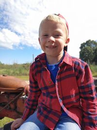 Portrait of smiling boy sitting on a tractor against blue sky with puffy clouds