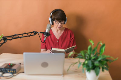 Young woman reading book sitting against wall