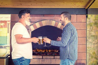 Multiracial male friends cooking meat on barbecue grill while drinking alcohol